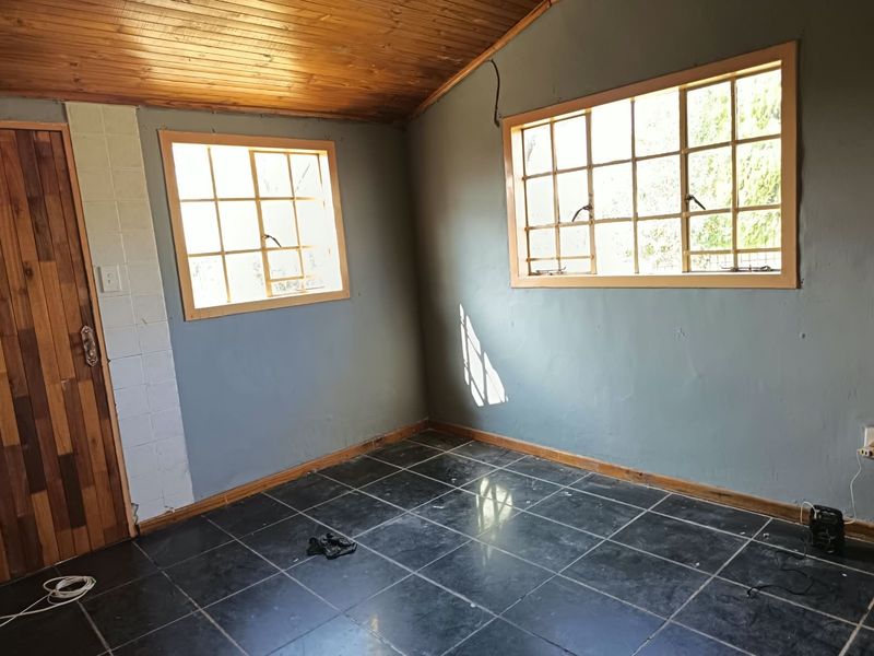 An empty bedroom featuring dark tiled flooring, a timber-clad ceiling, and wooden window frames, offering a blank canvas for renovation.