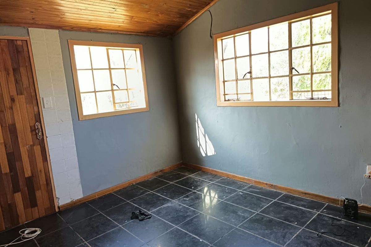 An empty bedroom featuring dark tiled flooring, a timber-clad ceiling, and wooden window frames, offering a blank canvas for renovation.
