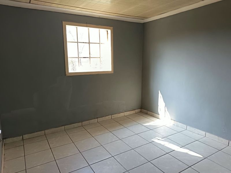 An empty bedroom featuring tiled flooring, a grid-pattern window, and a panel ceiling, offering a blank canvas for renovation or interior design.