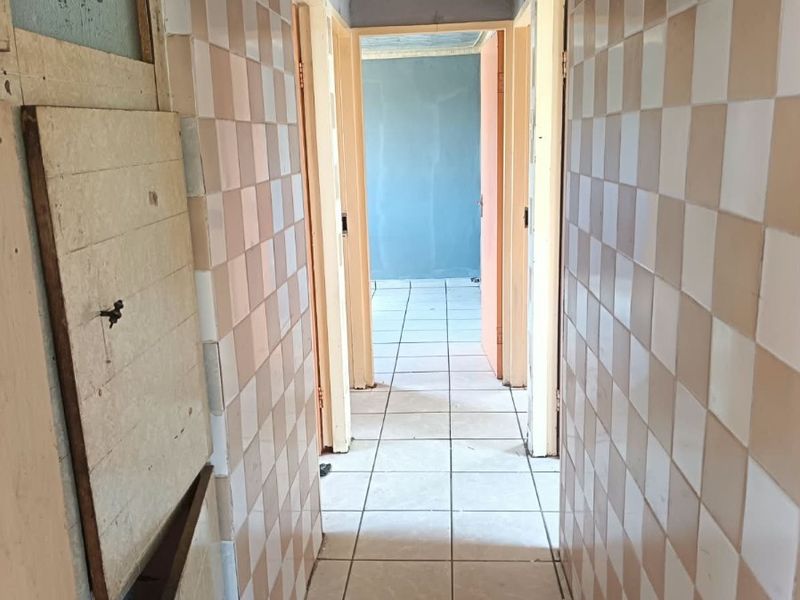 A narrow hallway featuring dated checkered wall tiles and ceramic floor tiles, requiring cosmetic updates and repairs to wall finishes and fixtures.