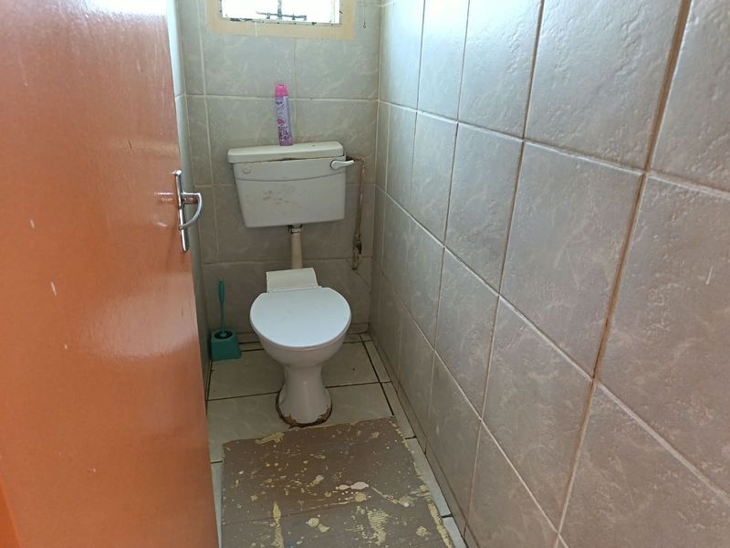 A compact bathroom featuring tiled walls and flooring, equipped with a standard toilet and a small window for ventilation.