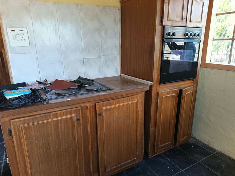 A dated kitchen featuring wooden cabinetry, a built-in oven, and an electric hob with tiled splashbacks and flooring.