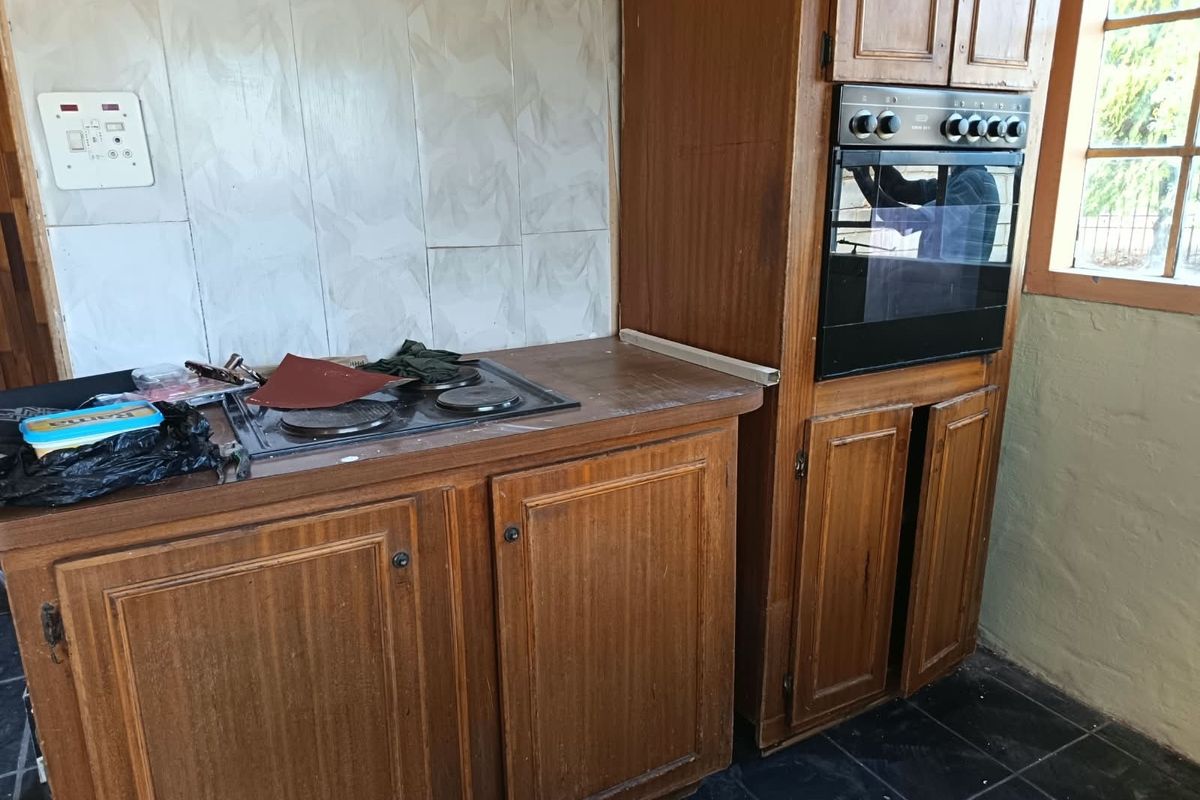 A dated kitchen featuring wooden cabinetry, a built-in oven, and an electric hob with tiled splashbacks and flooring.