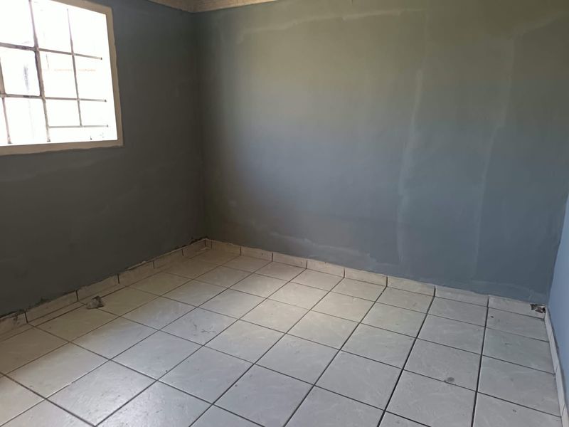 An empty bedroom featuring tiled flooring and a window with security bars, requiring minor cosmetic updates to the walls and flooring.