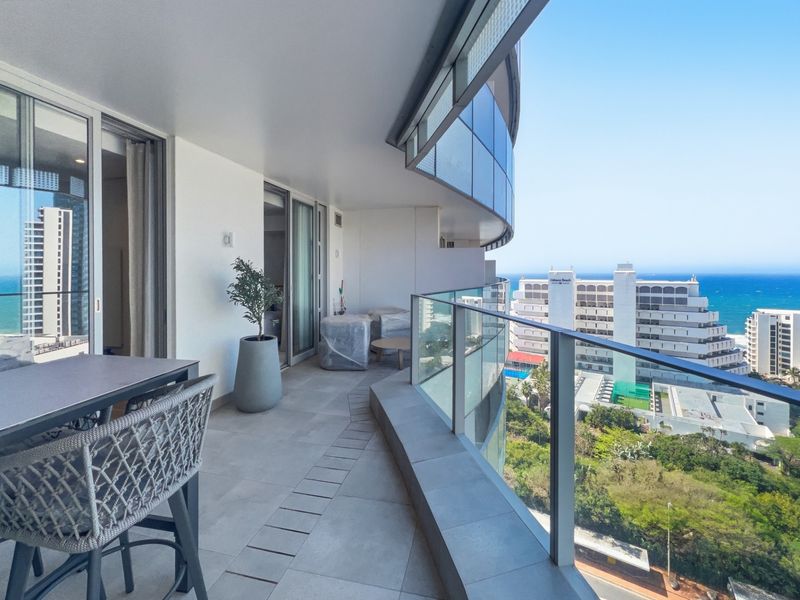 Spacious curved balcony featuring modern glass balustrades and tiled flooring, offering expansive coastal and urban views.