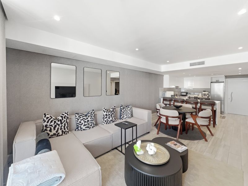 Modern open-plan living and dining area featuring a sleek kitchen with integrated appliances, recessed lighting, and ducted air conditioning in a well-maintained apartment.