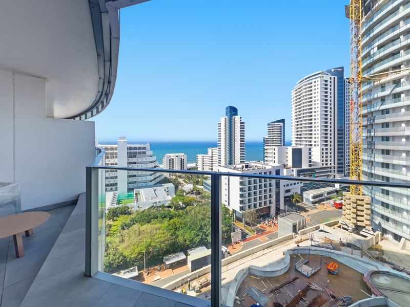 A modern balcony featuring a sleek glass balustrade and tiled flooring, offering expansive views of the surrounding city skyline and the ocean.