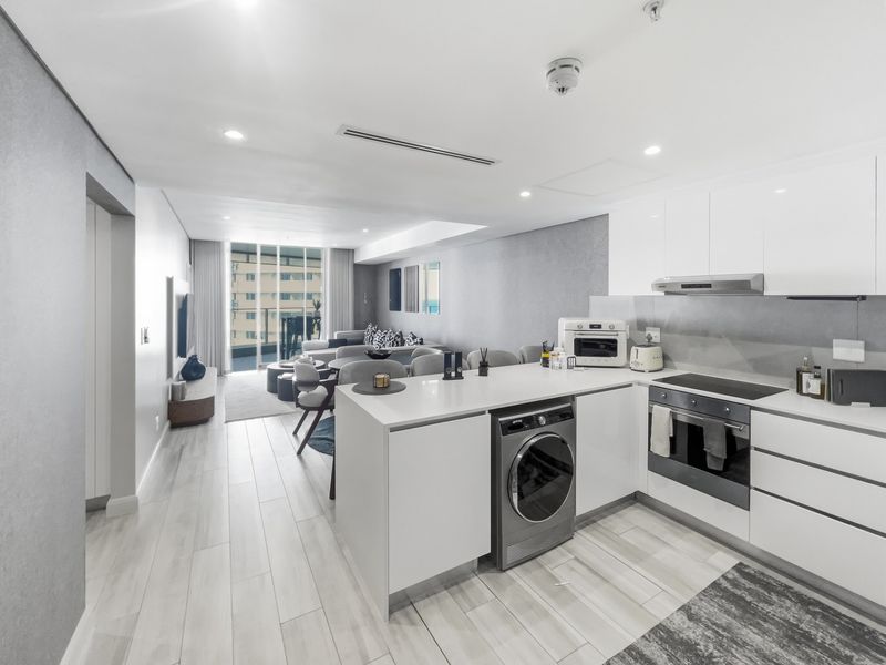 Modern open-plan living area featuring a sleek kitchen with integrated appliances, stone countertops, and seamless flow to the balcony through large sliding glass doors.