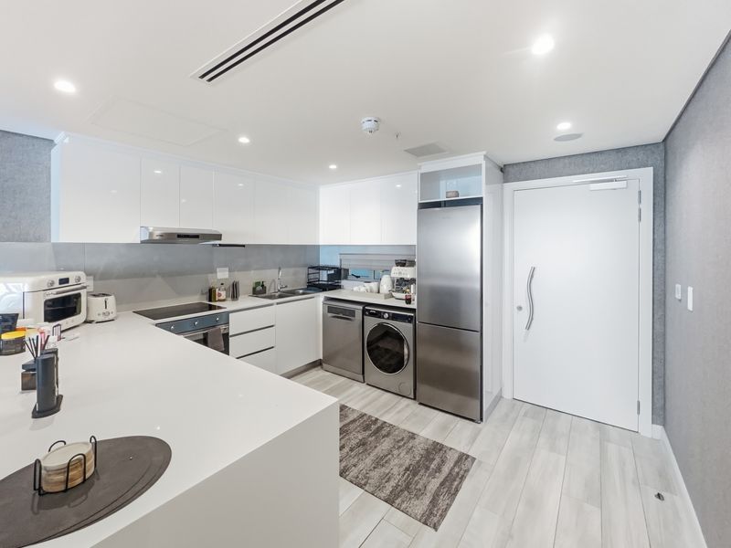 Modern kitchen featuring sleek white cabinetry, stone benchtops, integrated appliances, and a built-in laundry area, finished with recessed lighting and contemporary flooring.