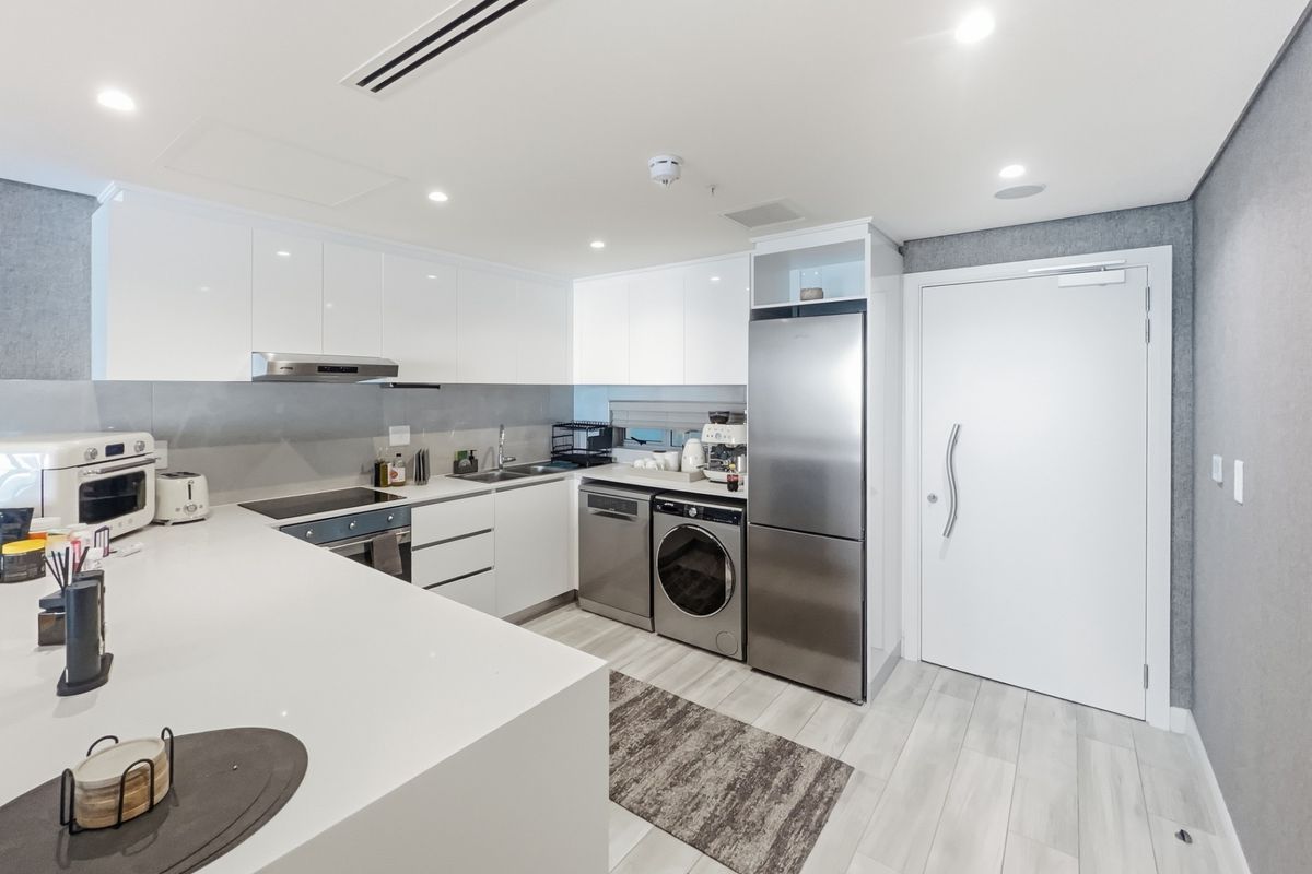 Modern kitchen featuring sleek white cabinetry, stone benchtops, integrated appliances, and a built-in laundry area, finished with recessed lighting and contemporary flooring.