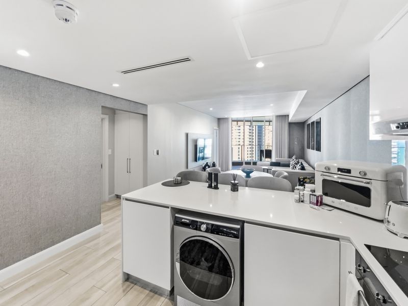 Modern open-plan apartment featuring a sleek kitchen with integrated appliances, stone island, and seamless flow into the living area with ducted air conditioning.