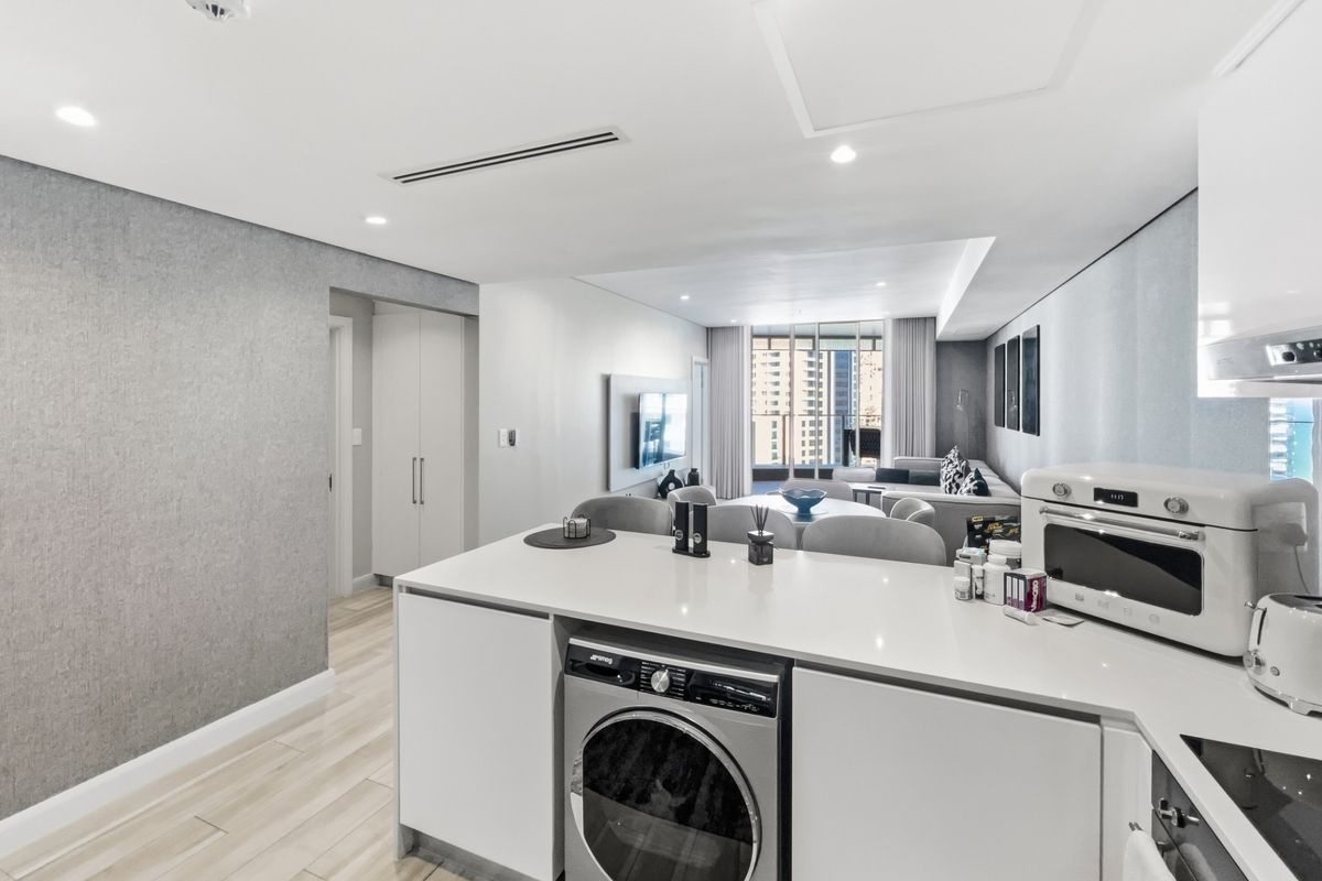 Modern open-plan apartment featuring a sleek kitchen with integrated appliances, stone island, and seamless flow into the living area with ducted air conditioning.