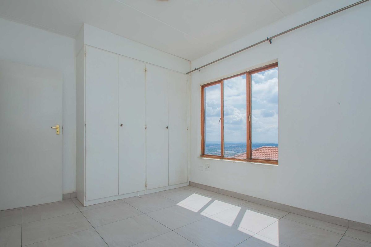 A bright, empty bedroom featuring tiled flooring, built-in cupboards, and a large window offering expansive views.