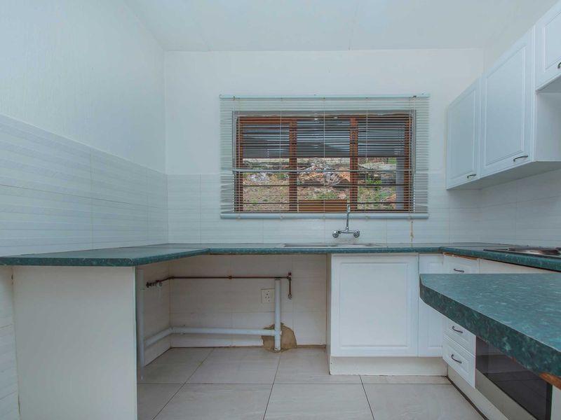 A functional kitchen featuring white cabinetry, green laminate countertops, tiled backsplash, and built-in oven, with visible plumbing connections ready for appliance installation.