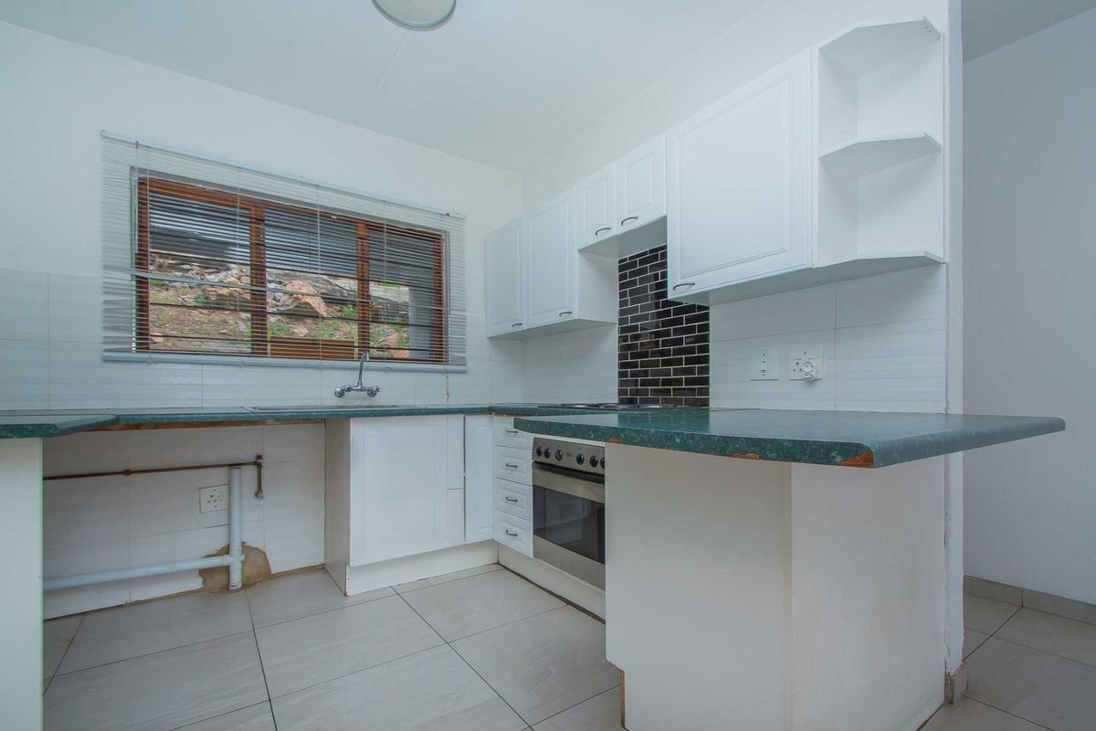 A functional kitchen featuring white cabinetry, a dark tiled backsplash, and a laminate countertop, currently awaiting final finishes and appliance installation.