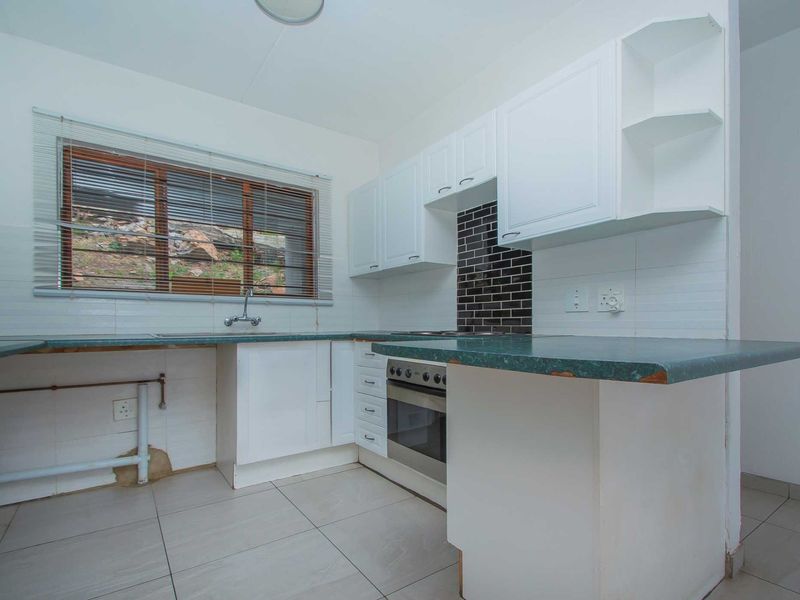 A functional kitchen featuring white cabinetry, a dark tiled backsplash, and a laminate countertop, currently awaiting final finishes and appliance installation.
