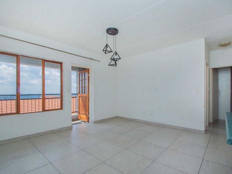 An empty open-plan living area featuring tiled floors, modern pendant lighting, and direct access to a balcony with scenic views.