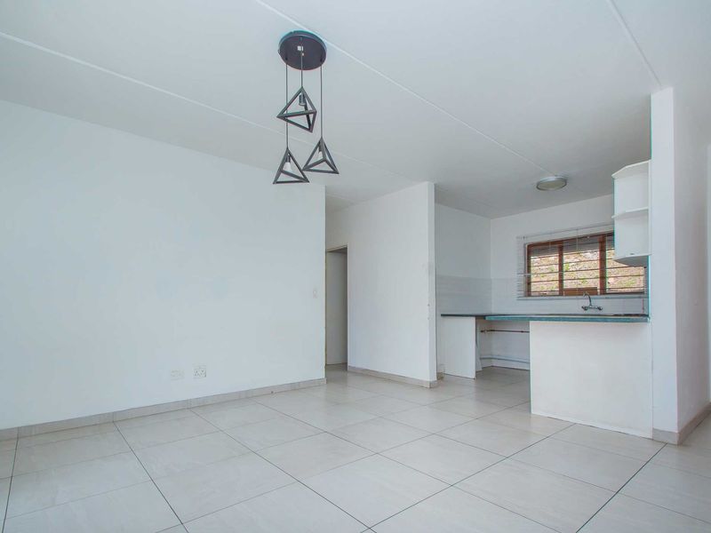 An open-plan living and kitchen area featuring neutral tiled flooring, built-in kitchen cabinetry, and a functional layout ready for personalization.