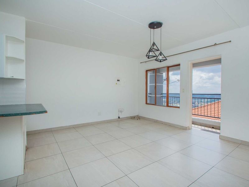 An open-plan living and kitchen area featuring tiled floors, modern pendant lighting, and direct access to a balcony with scenic views.