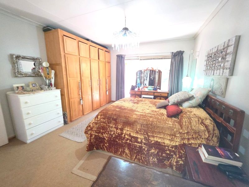 Spacious bedroom featuring extensive built-in wooden cabinetry, neutral carpeting, and natural light through a large window.