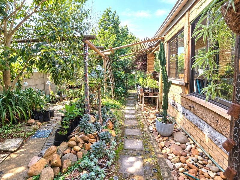 A landscaped rear garden path featuring a timber pergola, stone paving, and established garden beds alongside the brick exterior of the house.