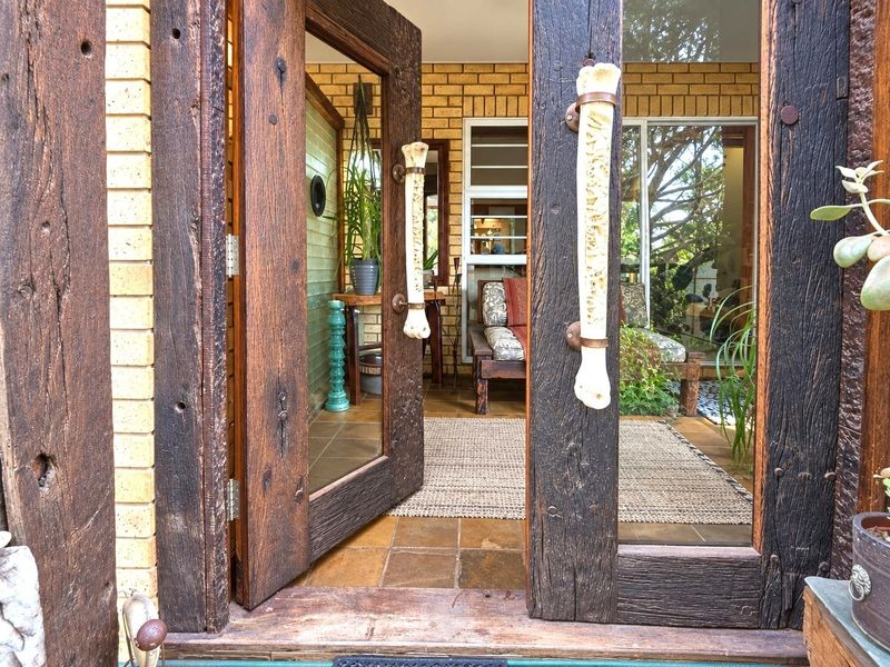 An inviting entrance featuring rustic timber-framed glass doors with unique custom handles, opening into a tiled foyer with exposed brick walls.