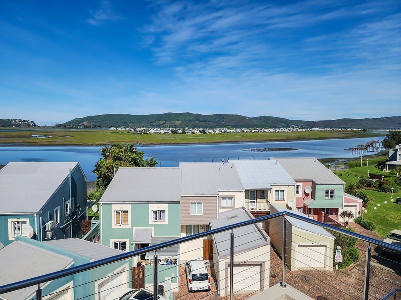 Elevated view overlooking a residential estate with a scenic lagoon and mountain backdrop, featuring modern metal roofing and stainless steel balcony railings.