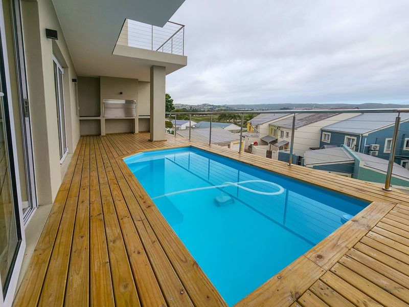 Elevated timber deck featuring a swimming pool, built-in braai, and modern glass balustrades with expansive neighbourhood views.