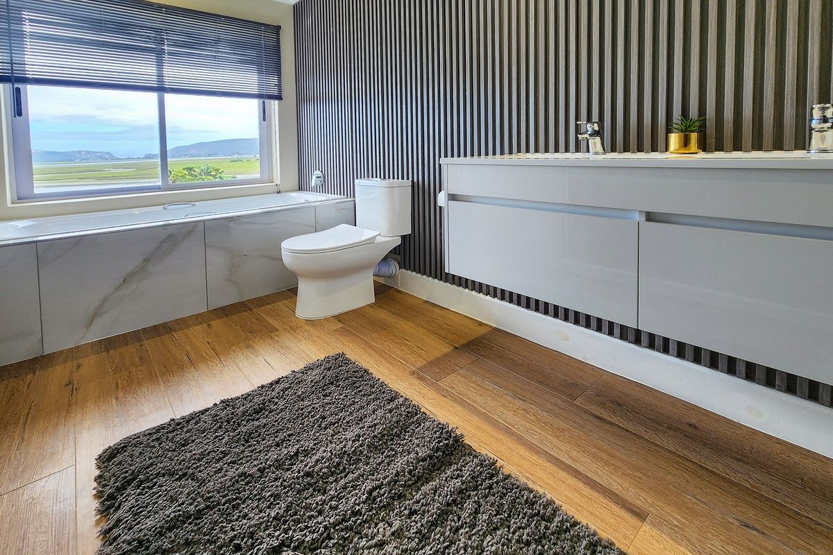 Modern bathroom featuring a built-in vanity, slatted wall paneling, a bathtub with scenic views, and high-quality laminate flooring.