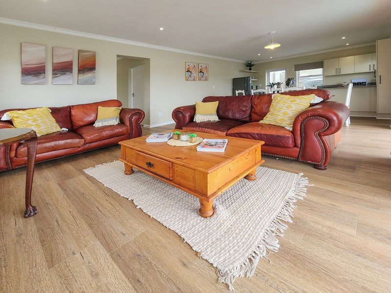 Spacious open-plan living area featuring modern laminate timber flooring, recessed downlighting, and a seamless transition into a functional kitchen space.