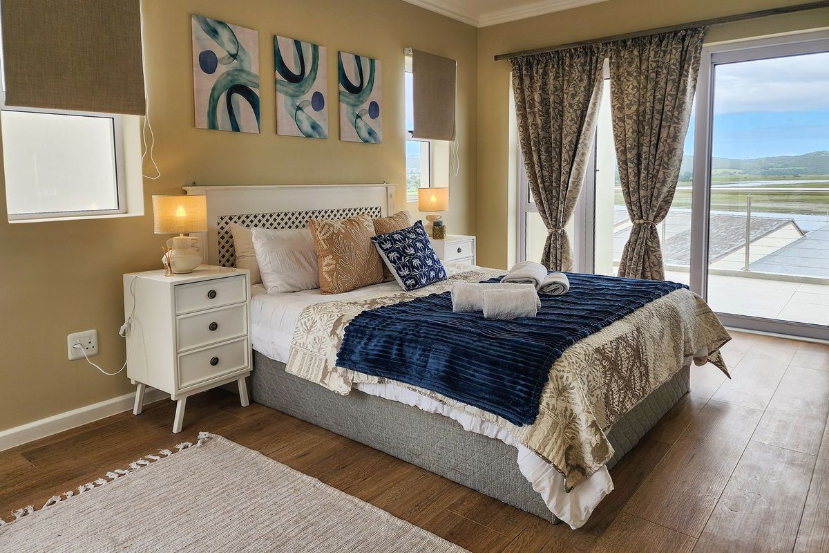 A well-maintained bedroom featuring laminate flooring, neutral wall tones, and a sliding glass door providing access to an outdoor balcony with scenic views.