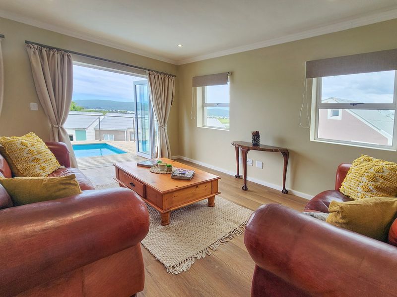 A bright living room featuring laminate flooring, recessed lighting, and double french doors opening onto a deck with a swimming pool view.