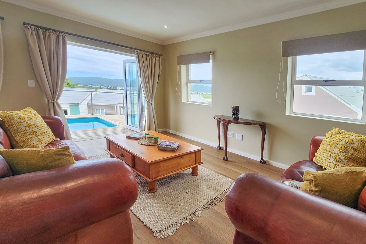 A bright living room featuring laminate flooring, recessed lighting, and double french doors opening onto a deck with a swimming pool view.