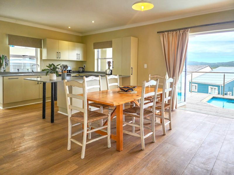 Open-plan kitchen and dining area featuring modern cabinetry, a central island, and direct access to an outdoor deck with pool views.