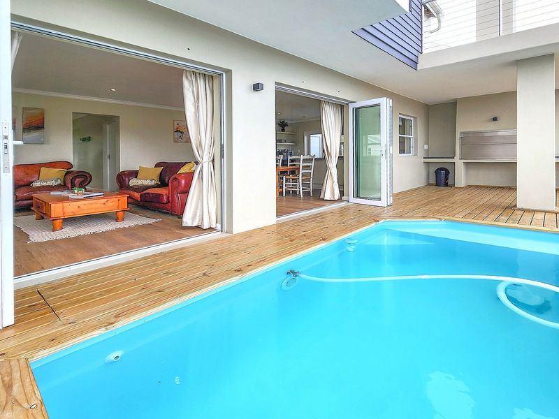 Outdoor entertainment area featuring a swimming pool, timber decking, and a covered patio with a built-in braai, seamlessly connected to the indoor living space.