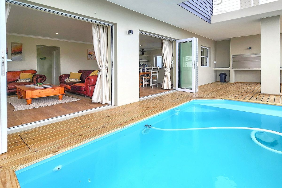 Outdoor entertainment area featuring a swimming pool, timber decking, and a covered patio with a built-in braai, seamlessly connected to the indoor living space.
