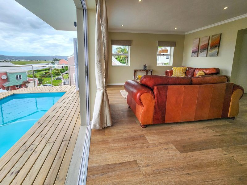 Open-plan living area featuring laminate flooring and large sliding doors opening onto a wooden deck with a swimming pool and scenic views.