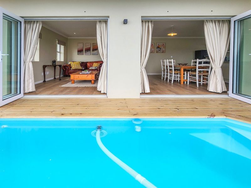 A well-maintained swimming pool with timber decking, featuring seamless indoor-outdoor flow through large bi-fold doors into the open-plan living and dining area.