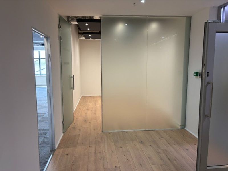 Modern office space featuring high-quality wood-look flooring, a sleek frosted glass partition, and contemporary recessed lighting.
