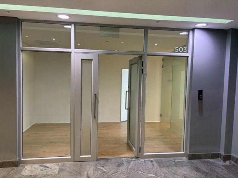 Modern office entrance featuring an aluminium framed glass door, glass partitions, and laminate flooring, providing a clean and professional aesthetic for the workspace.