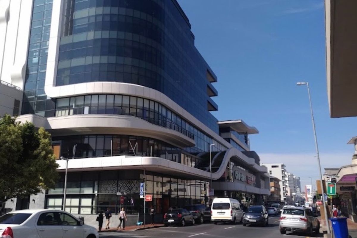 A modern multi-story office building featuring a curved glass facade and prominent street-level commercial frontage in a busy urban setting.