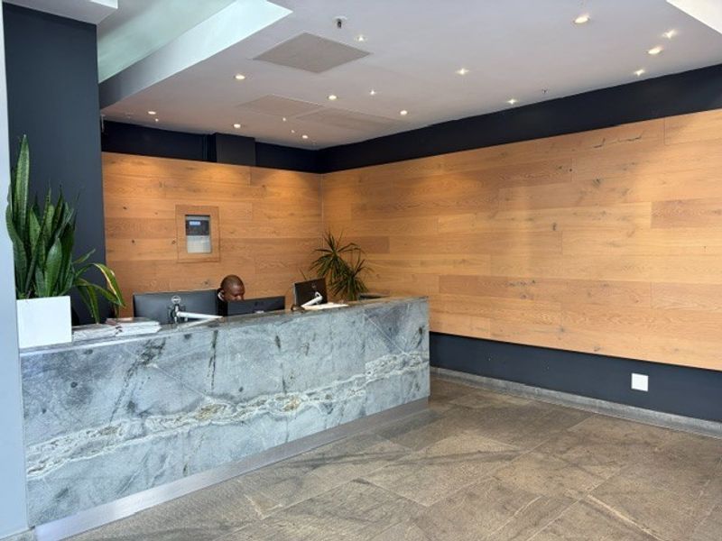 Modern office reception area featuring a premium stone desk, warm timber wall paneling, and high-quality stone flooring with recessed lighting.