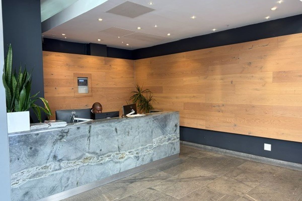 Modern office reception area featuring a premium stone desk, warm timber wall paneling, and high-quality stone flooring with recessed lighting.