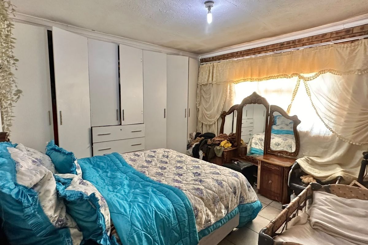 A bedroom featuring built-in cupboards and tiled flooring, showing signs of wear on the ceiling finish.