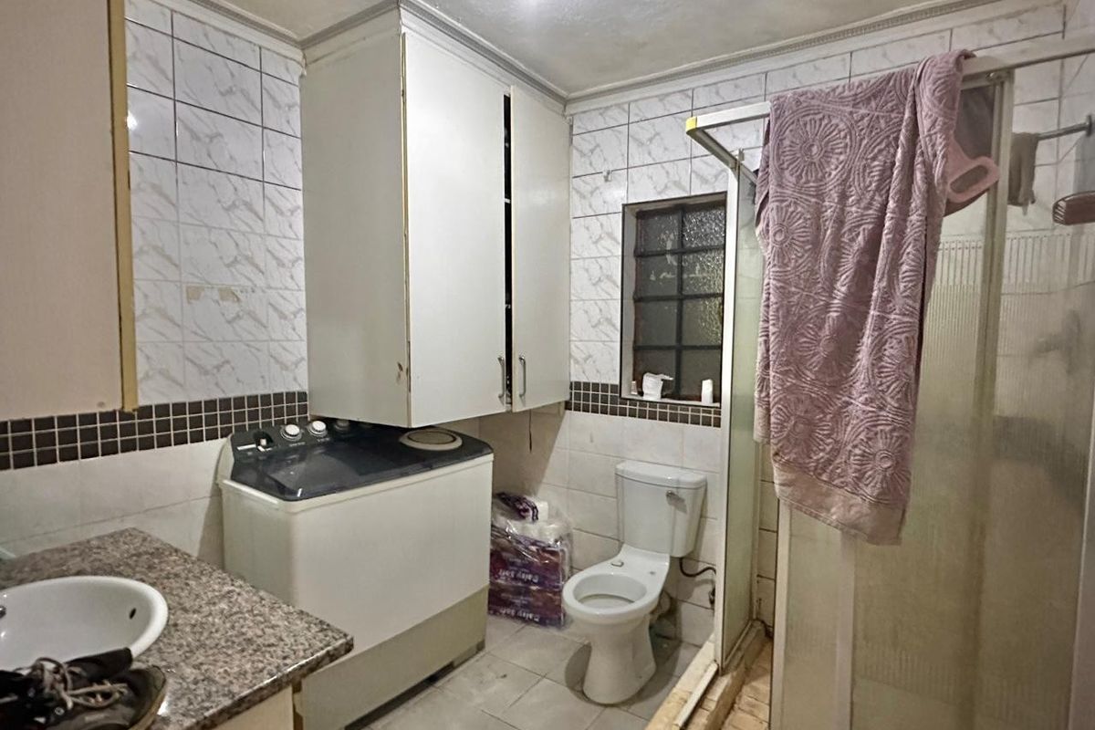 A functional bathroom featuring a shower enclosure, toilet, and vanity basin with granite countertop, requiring cosmetic updates to finishes and cabinetry.
