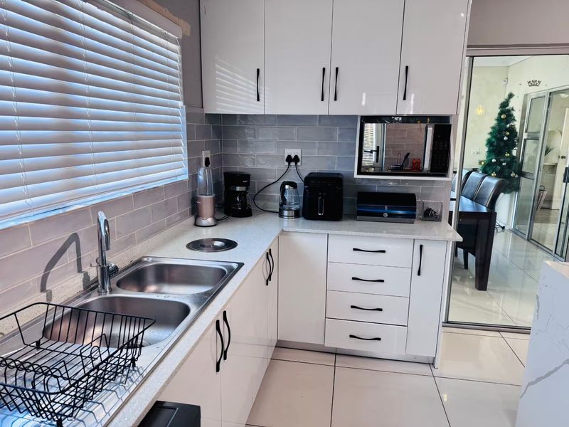 Modern kitchen featuring glossy white cabinetry, quartz countertops, subway tile backsplash, and a double bowl stainless steel sink with a mixer tap.