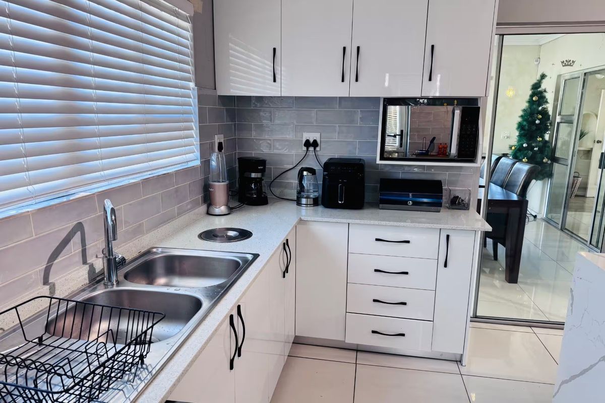 Modern kitchen featuring glossy white cabinetry, quartz countertops, subway tile backsplash, and a double bowl stainless steel sink with a mixer tap.