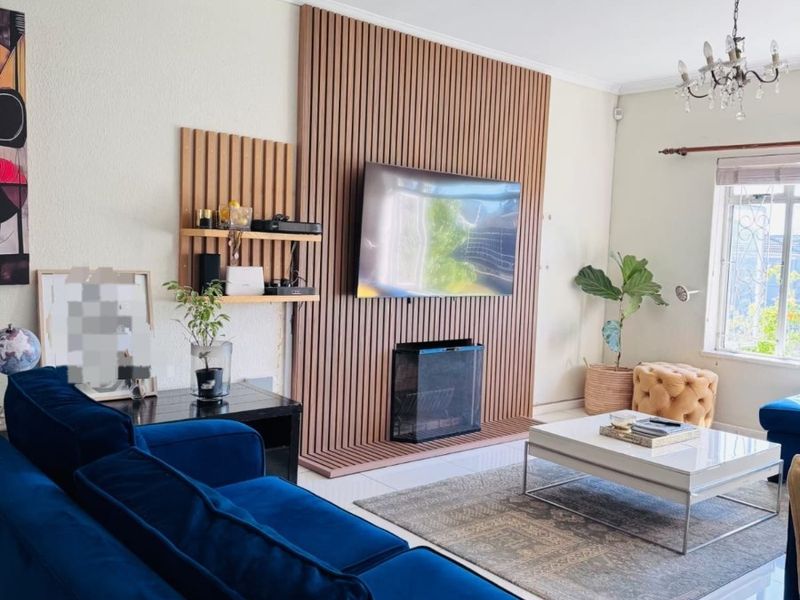 A well-maintained living room featuring a modern timber slat feature wall with an integrated fireplace and elegant chandelier lighting.