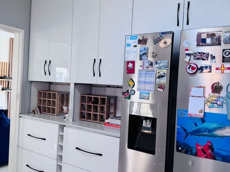 Modern kitchen area featuring high-gloss white cabinetry, stone countertops, and tiled flooring, providing ample storage and a clean, contemporary aesthetic.