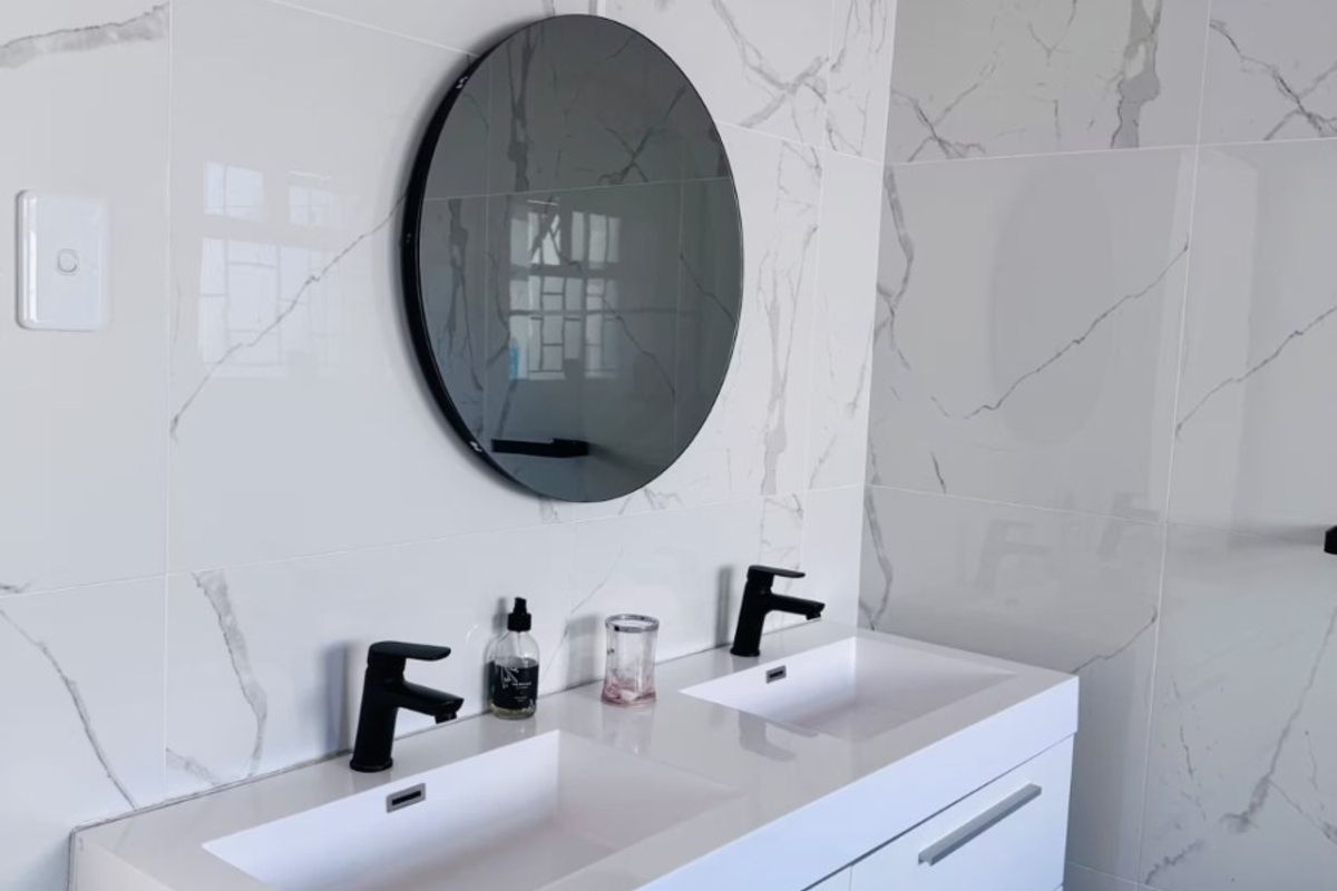 Modern bathroom featuring a sleek double vanity with integrated sinks, contemporary black fixtures, and elegant marble-look wall tiling.